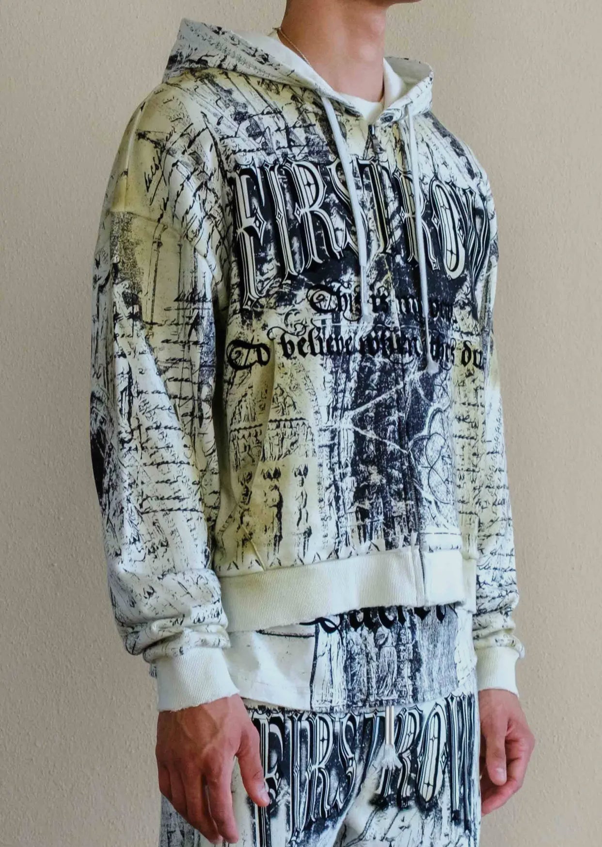 Person wearing a graphic hoodie and pants with text and design on a beige background